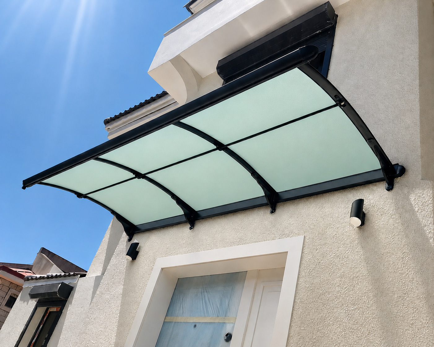 Curved frosted-glass canopy with black metal frame over a beige stucco doorway, blue sky in the background.