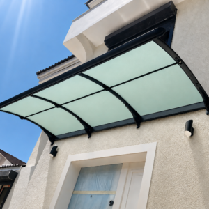 Curved frosted-glass awning with black metal frame above a beige stucco doorway against a clear blue sky