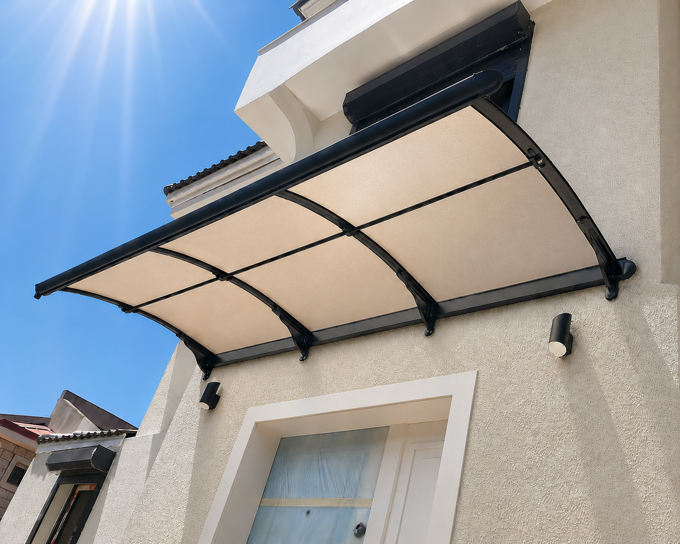 Beige house front with a curved translucent canopy over a white door framed by a black metal frame; clear blue sky and sun glare above.