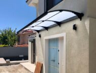 Beige stucco house exterior with a curved transparent polycarbonate canopy over a white-framed entry door.