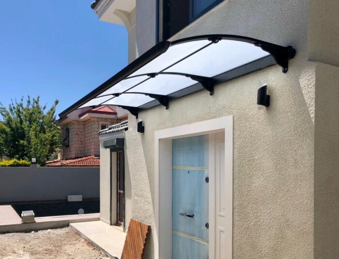 Beige stucco house exterior with a curved transparent polycarbonate canopy over a white-framed entry door.