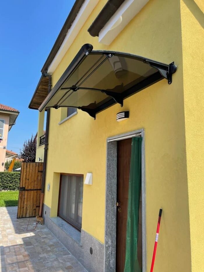 Yellow house exterior with a black glass canopy over a wooden door with stone frame