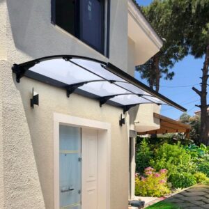 Glass and metal curved awning over a white front door on a beige stucco house, with a landscaped garden nearby.