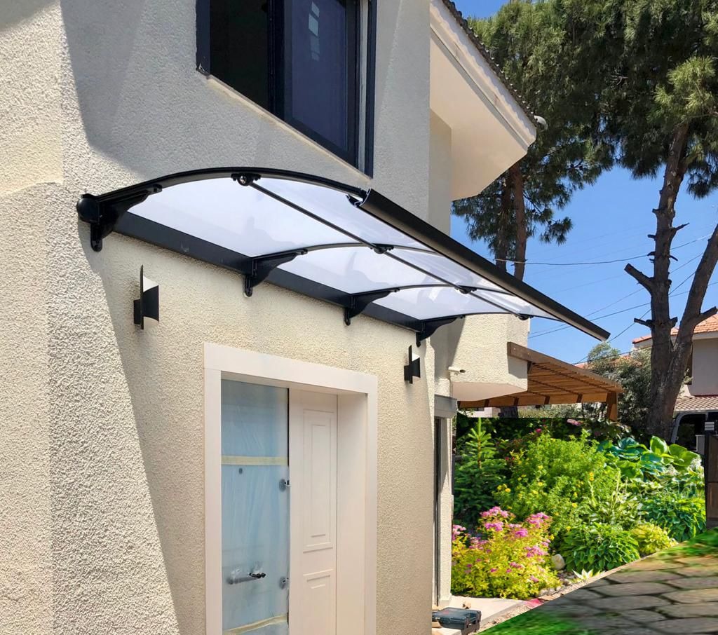 Glass and metal curved awning over a white front door on a beige stucco house, with a landscaped garden nearby.